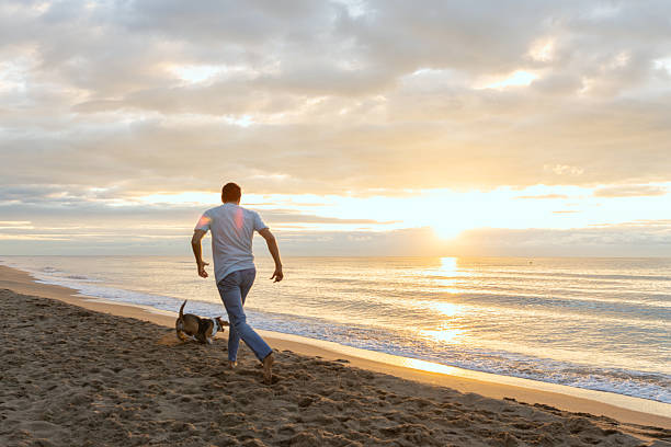 istock Man and dog running on beach during sunrise 2251256751