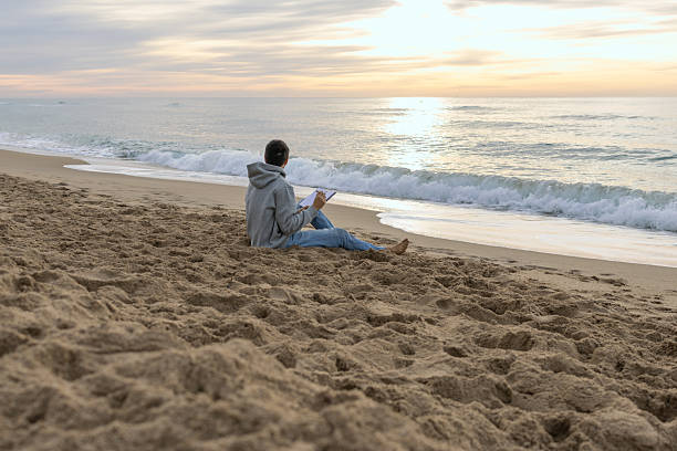 istock Man journaling on beach during ocean sunrise 2251256950