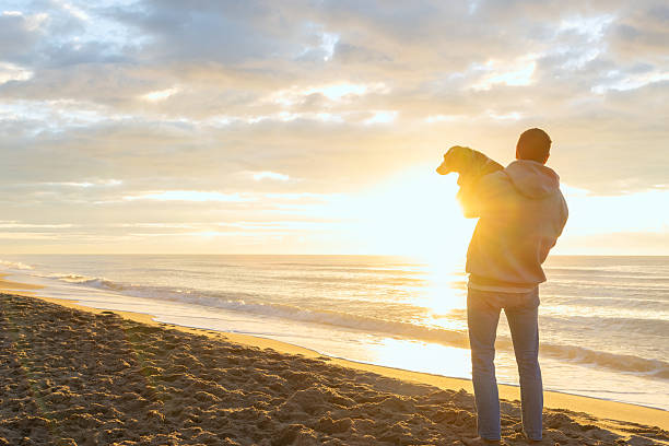 istock Man holding dog enjoying sunrise on beach 2251257255