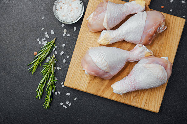 istock Raw chicken drumsticks on wooden board with herbs and spices 2251263428