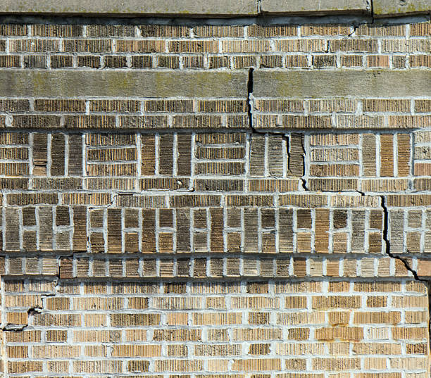 deep crack in brick building facade (crumbling infrastructure dangerous home) danger to pedestrians red brickwork repair needed brooklyn new york apartment house flats close up terra cotta cement