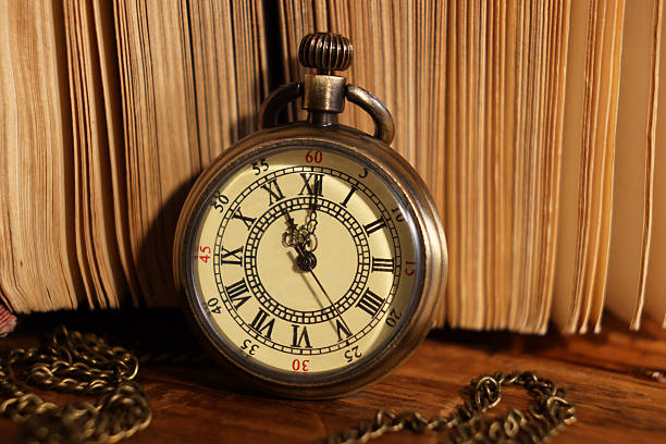 Pocket clock with chain and book on wooden table, closeup