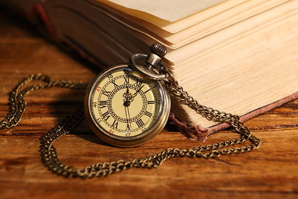 istock Pocket clock with chain and book on wooden table, closeup 2251269328