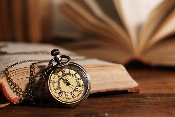 istock Pocket clock with chain and book on wooden table, closeup. Space for text 2251269348