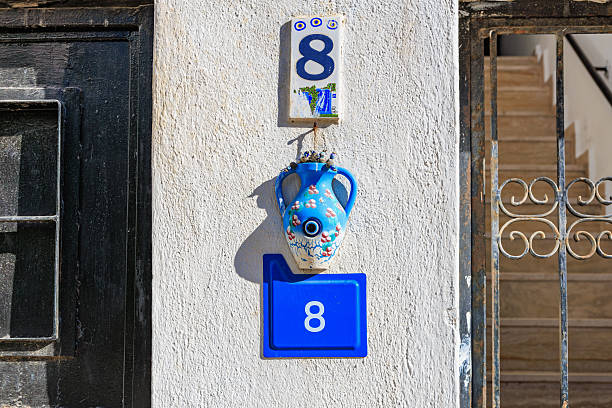 Decorative house number 8 on white wall with blue vase and evil eye amulet. August 5, 2025, Bodrum Turkey.