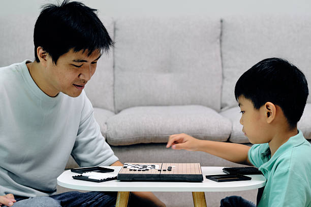 istock child placing a Go stone while an adult observes during a strategy game at home, highlighting logical thinking, concentration, and family bonding through a classic educational board activity 2251276432