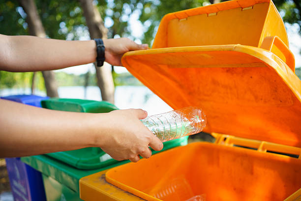 istock person throws a plastic bottle into an orange recycling bin outdoors. 2251280009