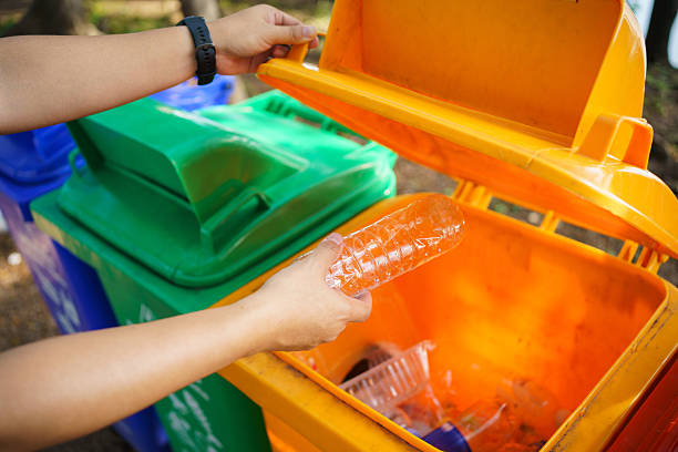 istock person throws a plastic bottle into an orange recycling bin outdoors. 2251280011