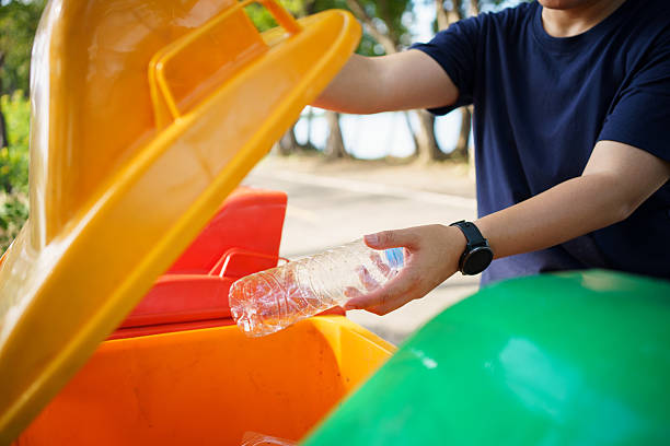 istock person throws a plastic bottle into an orange recycling bin outdoors. 2251280012
