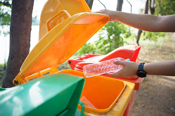 istock person throws a plastic bottle into an orange recycling bin outdoors. 2251280019