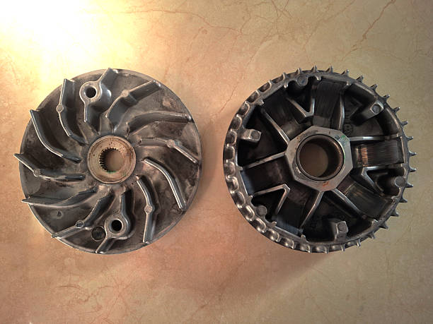 Close-up view of used metal parts from a scooter or automatic motorcycle's Continuously Variable Transmission (CVT) system, specifically the front variator/drive pulley (left) and the rear clutch bell/housing (right). These components regulate the gear ratio and power transfer for engine acceleration. Ideal for mechanical, engineering, maintenance, and vehicle repair contexts