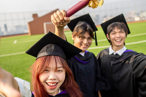 Graduate students celebrating with their degrees, wearing caps and gowns, and taking joyful selfies