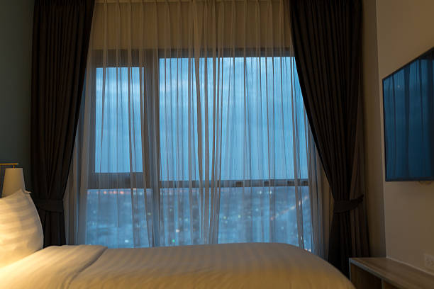 istock Bed and TV with sheer curtains, allowing light during dusk in a high building 2251283521