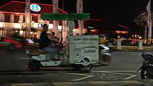 Surabaya, Indonesia – 10 October 2025: A three-wheeled coffee seller rides past, bringing a warm and lively street atmosphere with his mobile brew.