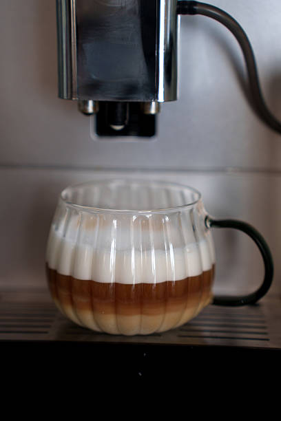 istock layered coffee in ornamented glass mug under metallic espresso machine with dark handle, showcasing creamy foamy top and rich brown layers in café setting, routine, breakfast, refreshing, enticing 2251289396