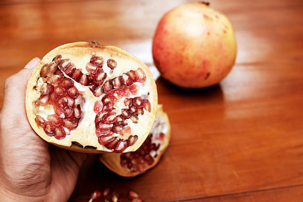 Broken ripe pomegranate in the hand over a wooden table, Pomegranates are juicy, sweet fruits with edible seeds called arils packed tightly inside.