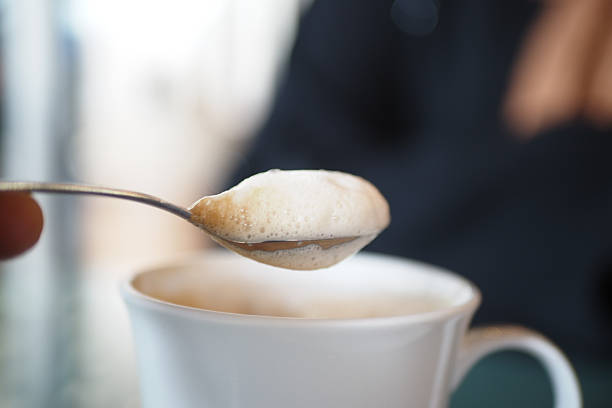 Person enjoys a spoonful of whipped cream over a cup of coffee.