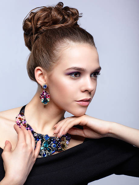 Brown-haired young woman in black dress and with bijouterie on gray background