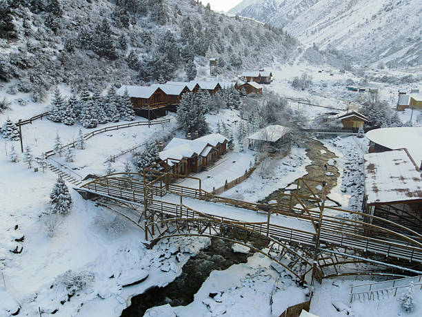 istock Snowy mountain resort cabins and rustic wooden bridge over a stream 2251300752