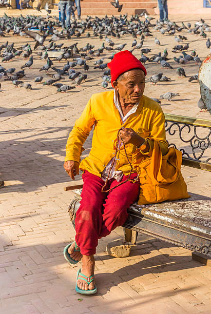 Rabat, Morroco - February 9th 2020: A traditionally dressed Moroccan woman sitting on a bench in front of an orange ancient wall with geometric holes