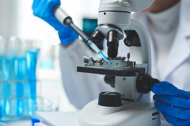 istock Close-up of gloved hands using a micropipette to place a blue liquid sample on a microscope slide for analysis in a modern laboratory with test tubes in the background 2251307622