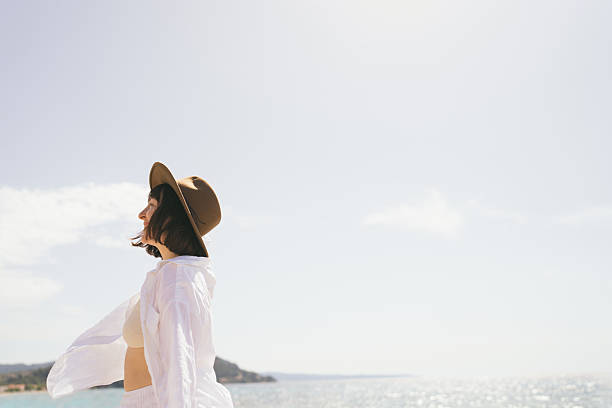 Photo of a young woman on her way to the local beach, wearing a hat and a linen shirt