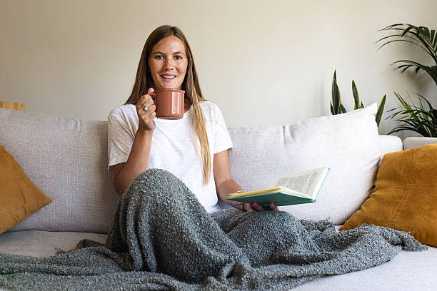 istock Young woman relaxing on sofa, reading and drinking tea 2251314320