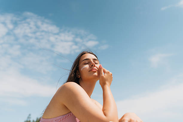 istock Young woman applying sunscreen on her face while at the beach 2251314538