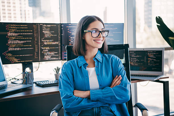istock Tech focused female programmer at a busy desk with multiple monitors in a modern office smiling confident 2251316555