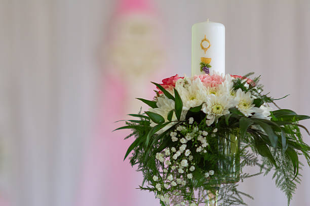 White Religious Candle Surrounded By Pink And White Flowers In A Soft Pastel Background, Designed For Ceremony Decoration And Elegant Event Atmosphere