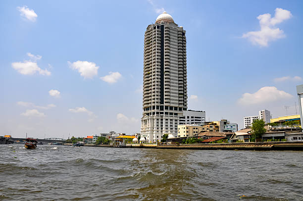 Dramatic Contrast in Architecture: Old Waterfront Homes and Dilapidated Buildings Against Modern Skyscrapers and Luxury Condos on the Chao Phraya River in Bangkok, Thailand