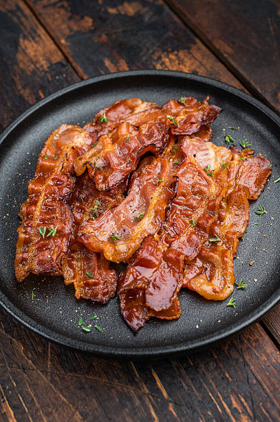 istock Crispy sizzling bacon with glossy caramel surface served on a dark plate over rustic wood creating rich appetizing food style. 2251324162