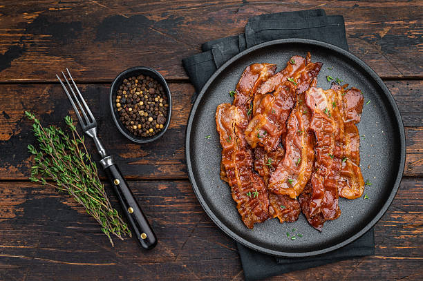 istock Crispy fried bacon arranged on a black plate over rustic wood offering deep color, shine and high-impact gourmet atmosphere. 2251324536