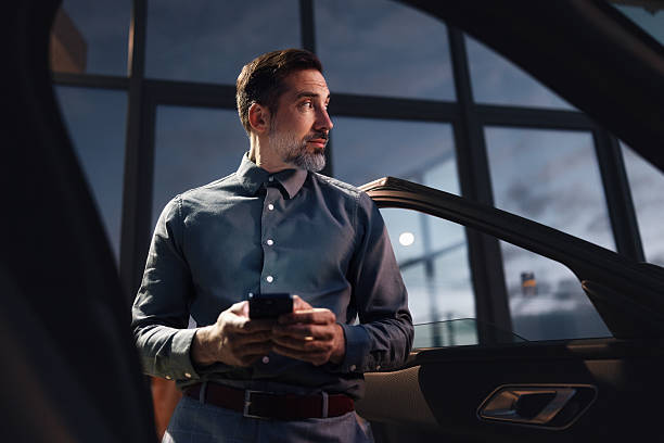 istock Businessman Using Smartphone In Modern Office At Night, Waiting Beside Elevator Near Glass Windows Interior 2251332206