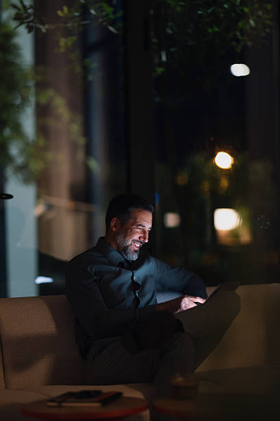 istock Smiling Man Relaxing on Couch at Night Using Tablet in Modern Home Setting 2251332227