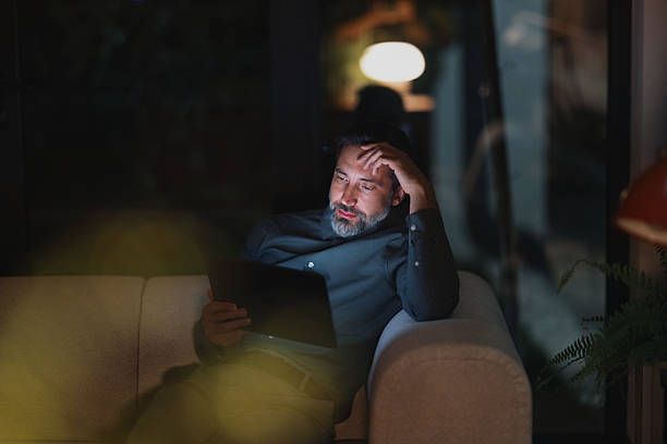 istock Relaxed Businessman Reading Tablet At Night On A Sofa In A Modern Home Office Setting 2251332230