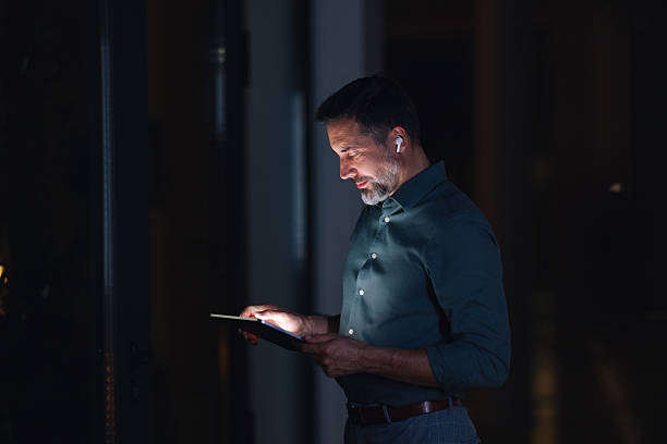 istock Professional Man Using Tablet At Night In Dim Office Setting With Earbuds 2251332295