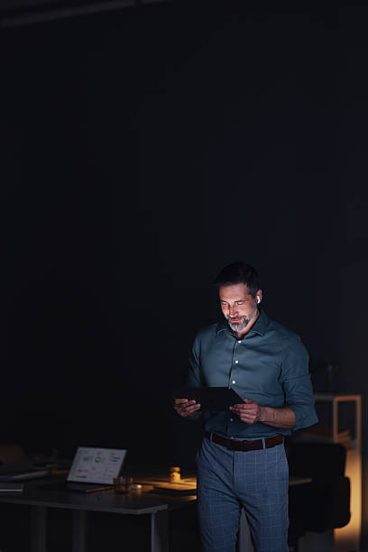 istock Professional Man Working Late in Dim Office With Tablet and Earbuds at Night 2251332309