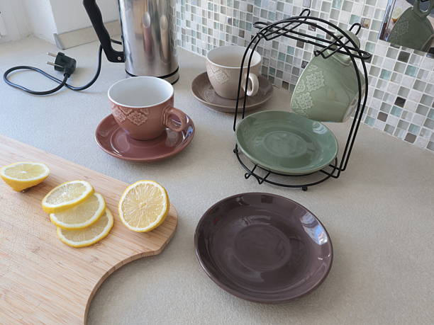 Ceramic cups and sliced lemon on wooden cutting board. Tea and cooking in kitchen. Food and drinks. Set of dishes on stand.