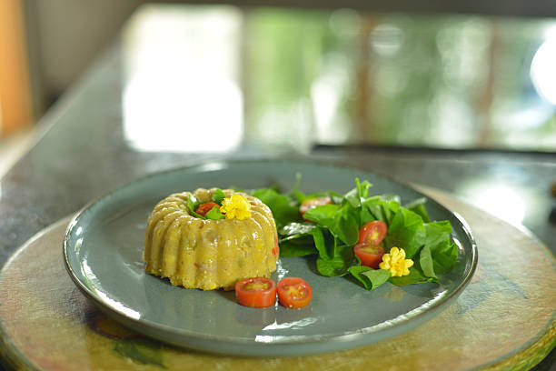 Close-up of a mini Brazilian cuscuz paulista on an individual plate, decorated with egg, cherry tomato, and greens. Natural light highlights vibrant colors and texture, conveying freshness and culinary appeal, perfect for Brazilian food photography