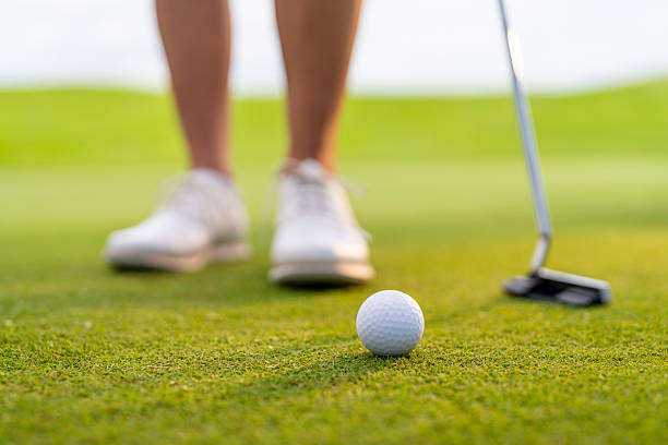 A close-up shot shows a woman golfer intently preparing to putt on the green, with her putter and the golf ball clearly visible. The close-up captures her concentration as she aims for the hole, highlighting her determination and focus on the sport.