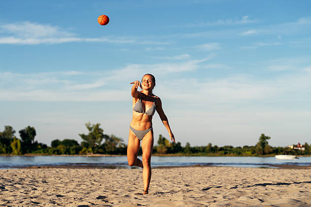 istock Active woman throwing a ball on the sandy beach during summer vacation 2251340273