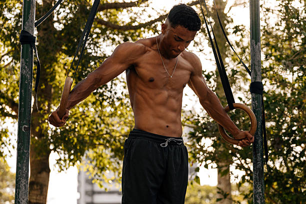 Athlete performing a controlled ring support hold during calisthenics training in an outdoor park. Strength, balance, focus, and athletic physique