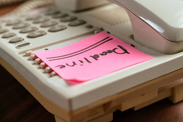 Close up of a retro office phone with a pink sticky note labeled Deadline on wooden desk.