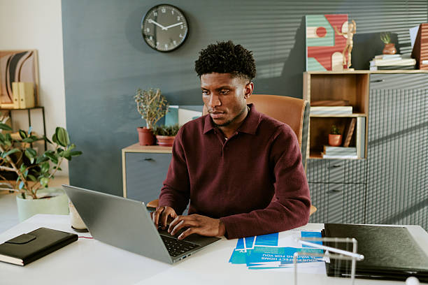 istock Young Adult Black Man Working on Laptop in Modern Office Environment 2251346882