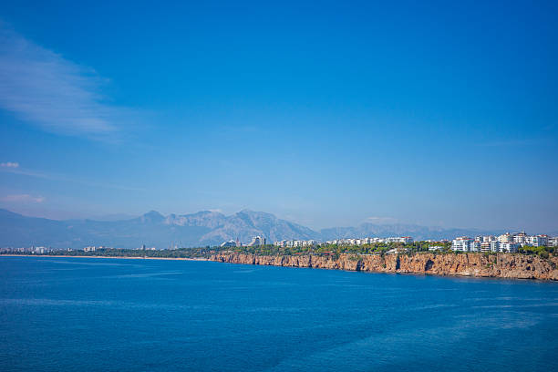A breathtaking panoramic view of the Mediterranean coastline featuring deep blue ocean waters, rugged cliffs, and a distant cityscape nestled beneath a majestic mountain range. Clear skies and vibrant natural colors create a serene and captivating summer atmosphere, ideal for travel marketing, tourism campaigns, destination promotions, and scenic landscape publications