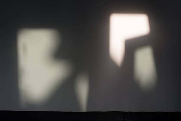 An abstract, out-of-focus image of geometric light shapes projected onto a dark wall, creating a mysterious and moody background texture. Representing hope, clarity, or architectural detail