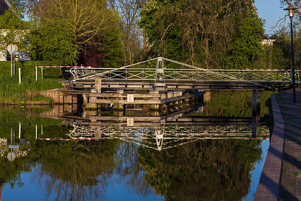 A bridge over a river with a reflection of the bridge in the water. The bridge is old and has a rustic appearance. The water is calm and peaceful
