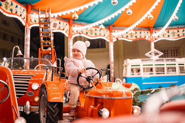 A child sits on a toy tractor on a vintage carousel at a winter fair, surrounded by colorful lights and decorations. Captures playful childhood moments and festive outdoor entertainment. Great for themes of nostalgia, tradition, and family activities.