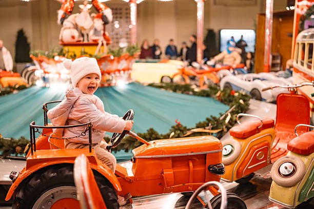 A young child laughs with excitement while riding a vintage orange tractor on a holiday carousel. Bright illumination adds a magical winter fair ambiance.